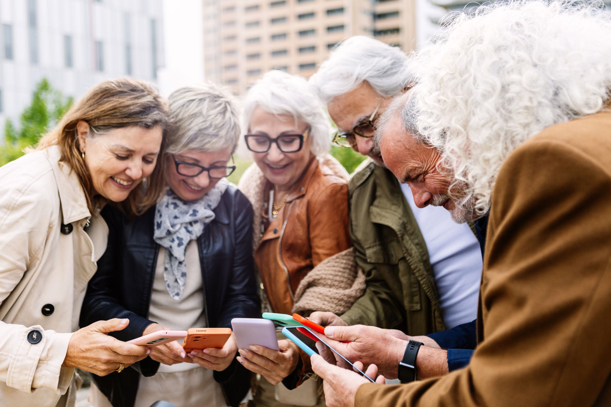 Groupe de personnes retraitées qui utilisent l’appareil mobile et qui se tiennent en cercle à l’extérieur.